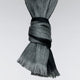 A gray and black woven scarf is tied in a knot, displaying its fringed ends against a plain, light-colored background.