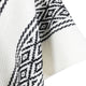 A white woven textile features a black geometric pattern along the edge, creating a striking contrast. The fabric drapes softly, highlighting the intricate design in a close-up view.