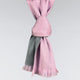 A two-toned scarf, pink and gray, is tightly knotted and hangs with fringed ends against a plain background.
