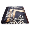 A folded blanket displaying geometric patterns in blue, white, and beige rests against a plain background, revealing its intricate design through partially layered edges.