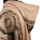 A tan fabric coat features a large hood and intricate dark geometric patterns, draping over a mannequin. The design blends soft textures with bold motifs in a studio setting.