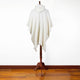 A white hooded cape drapes over a wooden stand, displayed in a room with polished wood floors and a plain white wall.
