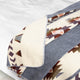 Blanket with geometric patterns lies spread out on a bed, showcasing designs in earthy tones of brown, grey, and cream, creating a warm and cozy atmosphere.