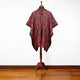 A red and black patterned poncho is displayed on a wooden stand, set against a white background and brown wooden floor.