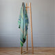 Sucua baby alpaca wool blanket – a wooden coat stand holds a striped green blanket. It stands on a parquet floor against a light gray wall in a minimalist room
