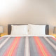 Ajilanga baby alpaca wool blanket – a bed is neatly made with a striped blanket in red, orange, and gray tones, flanked by two bedside lamps in a softly lit, neutral-colored bedroom