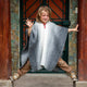 Zuleta llama wool hooded poncho – child wearing a grey poncho engages in playful balancing between two wooden pillars, with a decorative stone wall and glass door in the background