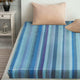 Pululahua baby alpaca wool blanket – a bed with a blue striped sheet is neatly arranged, topped with beige pillows. It is situated next to a white bedside table holding a decorative lantern, within a cozy room