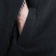 A hand rests inside a dark, textured fabric cloak, with embroidered details at the torn edge, creating a mysterious and intimate atmosphere.