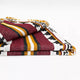 A folded, woven blanket displays bold geometric patterns with burgundy, mustard yellow, black, and white stripes. It rests against a plain white background.