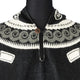A black wool sweater with a white spiral pattern is buttoned at the collar. The design includes geometric shapes, set against a plain backdrop.
