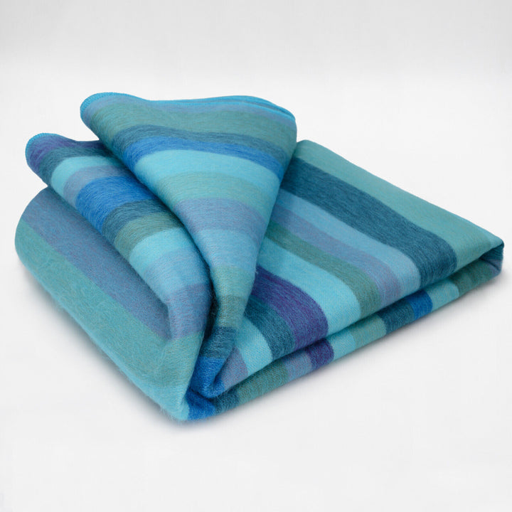Pululahua baby alpaca wool blanket – a folded, striped blanket displays shades of blue and green, resting on a plain white surface
