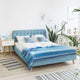 Pululahua baby alpaca wool blanket – a blue upholstered bed is neatly made with white bedding and blue accents, in a bright room adorned with plants, a wooden nightstand, art on the walls, and striped blanket