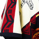 A fabric features bold geometric patterns in red, black, and cream. Triangular and linear designs create a visually striking appearance. The texture suggests a woven material in an abstract style.