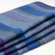 Morona baby alpaca wool blanket – woolen blanket folded neatly, featuring soft horizontal stripes in shades of blue, purple, and grey, resting on a plain white surface