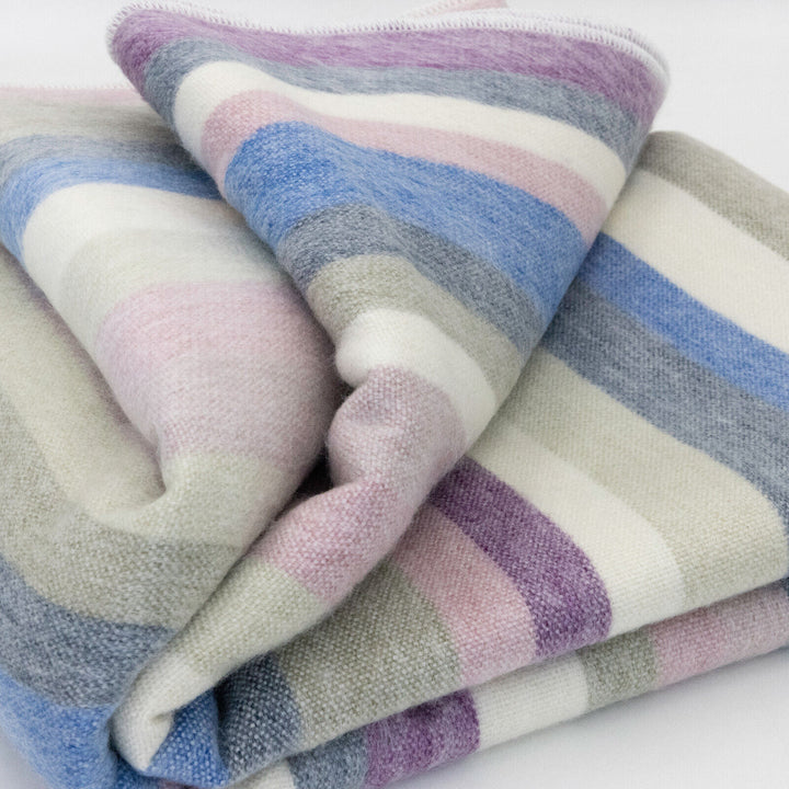 Yunga baby alpaca wool blanket – a soft, multi-colored striped blanket is neatly folded, displaying shades of blue, pink, purple, and gray against a white background