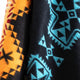 A close-up of fabric displays vibrant geometric patterns. The left side features orange, red, and black triangles, while the right side shows blue and black designs with star-like shapes.