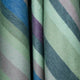 Imbabura baby alpaca wool blanket – fabric rolls display diagonal stripes in shades of green, blue, purple, and gray, creating a soft, woven texture. The tightly rolled fabrics suggest potential use for design or tailoring