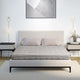 Bed with patterned gray bedding and two pillows, situated between two nightstands with lamps. A geometric artwork hangs above in a minimalistic bedroom setting.