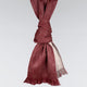 A maroon woven scarf is knotted, with fringe at both ends, draped against a plain light gray background.