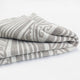 A folded blanket features a beige and white geometric pattern, resting neatly against a plain, white background.