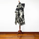 A mannequin displays a black cloak adorned with white horse illustrations, standing in a minimalist room with wooden flooring and a plain white background.