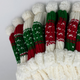 Knit stockings with red, green, and white patterns hang in a row on a white background, topped with fluffy white cuffs and pom-poms, conveying a festive holiday theme.