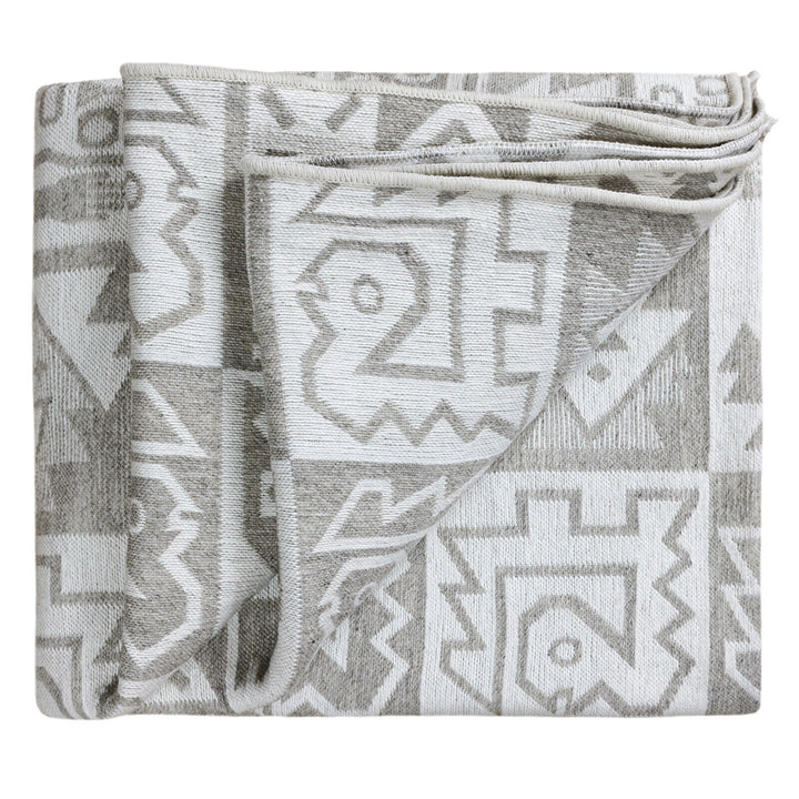 A folded blanket displaying a geometric pattern in gray and white rests against a plain background, highlighting its intricate, symmetrical design.