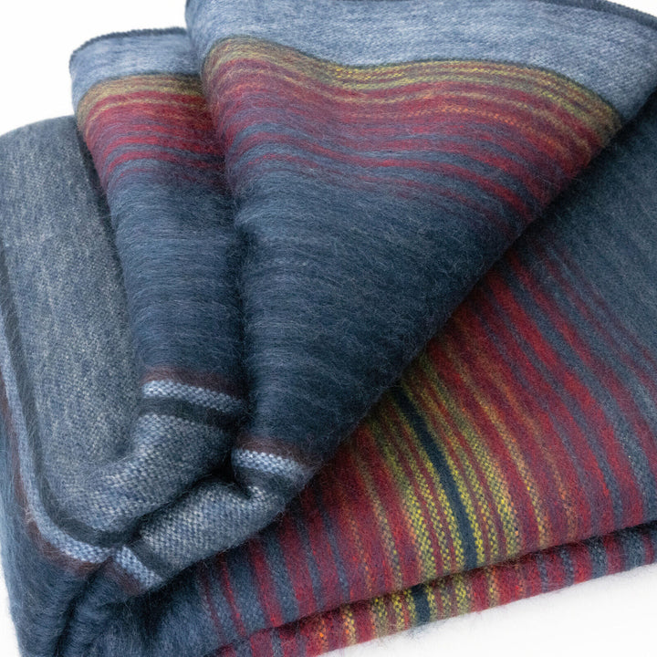 Huasaga baby alpaca wool blanket – a folded woolen blanket displays a rich pattern of blue, red, and yellow stripes, lying on a flat white surface, emphasizing its soft texture and vibrant colors