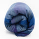 Morona baby alpaca wool blanket – a wool blanket, rolled up tightly, displays gradient shades of blue and purple. It rests on a plain white background