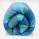 Pululahua baby alpaca wool blanket – a rolled-up blanket, featuring a soft, multicolored gradient of blues and purples, rests against a plain white background