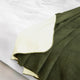 A dark green and cream-colored blanket lies partially folded on a white sheet, displaying its dual-colored layers in a smooth, cozy arrangement.
