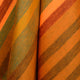 Putumayo baby alpaca wool blanket – the fabric features warm, diagonal stripes in shades of orange, brown, and green, creating a vibrant and cozy appearance. It is folded in overlapping layers