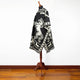 A black and white poncho, featuring a rearing horse design, is draped over a wooden mannequin stand. The scene is set against a plain white wall and wooden floor.