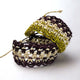 Two crochet bracelets, showcasing intertwined earthy tones of brown, cream, and olive green, rest against a plain white background, displaying their detailed, open-weave pattern.