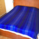Chibuleo baby alpaca wool blanket – a bed is covered with a blue-striped blanket, resting in a wooden bedroom setting with a headboard. A dresser with drawers is visible to the left