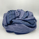 Chimborazo baby alpaca wool blanket – a folded blue blanket with horizontal stripes rests on a plain, light gray background. The blanket features varying shades of blue, adding texture and color contrast to the soft fabric