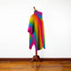 A colorful striped poncho is draped on a mannequin stand in a room with wooden floors and a white wall.