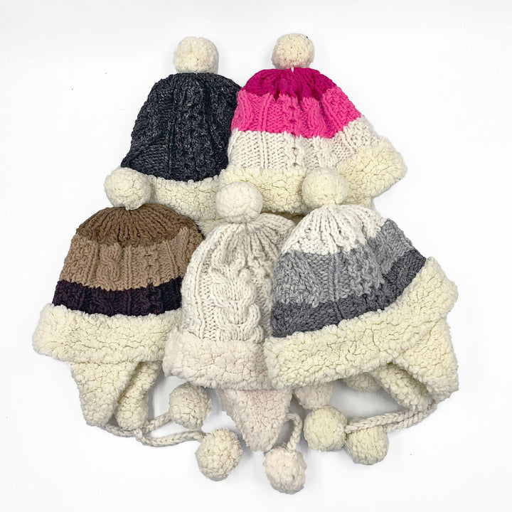 Five knit winter hats with pom-poms and fluffy edges are displayed. The hats feature different color patterns, including gray, pink, brown, and cream, set against a white background.