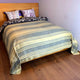 Chalua baby alpaca wool blanket – a bed with a wooden headboard features striped bedding and decorative pillows with floral and geometric patterns, set in a room with light-colored walls and hardwood flooring