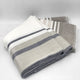 Yacoubina baby alpaca wool blanket – folded woolen throw blankets display gray, white, and beige horizontal stripes. They rest on a white surface, creating a soft and cozy appearance