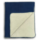 A two-toned blanket, primarily navy blue with an ivory underside, has one corner folded over, displaying both colors. The texture appears soft, resting against a plain, white background.