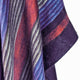 A close-up of a multicolored woven fabric displays wavy stripes in blue, purple, red, and gray hues, showcasing its textured and layered appearance.