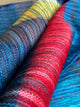 Alpaca wool queen blanket – colorful woven fabric rolls display vibrant patterns with dominant reds, blues, and yellows. They are closely stacked, showing intricate textures and a rich blend of colors in a textile setting