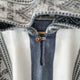 Palora lightweight alpaca wool hooded poncho – a woven fabric with a mix of gray, white, and beige patterns features a single button closure on a vertical slit. The background shows a wooden hanger