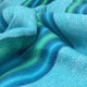 Machay baby alpaca wool blanket – a close-up of soft, blue wool fabric adorned with green and dark blue stripes, draped in gentle folds, creating a cozy, textured appearance