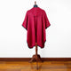 A red hooded cape hangs on a wooden mannequin stand, set against a plain white wall and a wooden floor background.