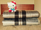 Quisapincha baby alpaca wool blanket – a plush Hello Kitty toy with a red bow sits atop two folded striped blankets on a bed, with a wooden headboard in the background