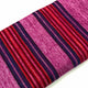 Cayetana baby alpaca wool blanket – a textured, colorful textile with alternating vertical stripes in pink, red, and dark purple, rests on a white background, highlighting its vibrant pattern and smooth fabric surface