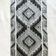 Cuyuja lightweight alpaca wool hooded poncho – a patterned textile features a series of geometric, diamond-shaped designs in shades of gray. The intricate pattern runs vertically on a soft, textured, off-white background